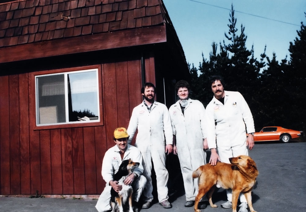 Four people and two dogs stand outside of a shop in an old photo.
