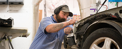 A person carefully inspects the front end of a car.